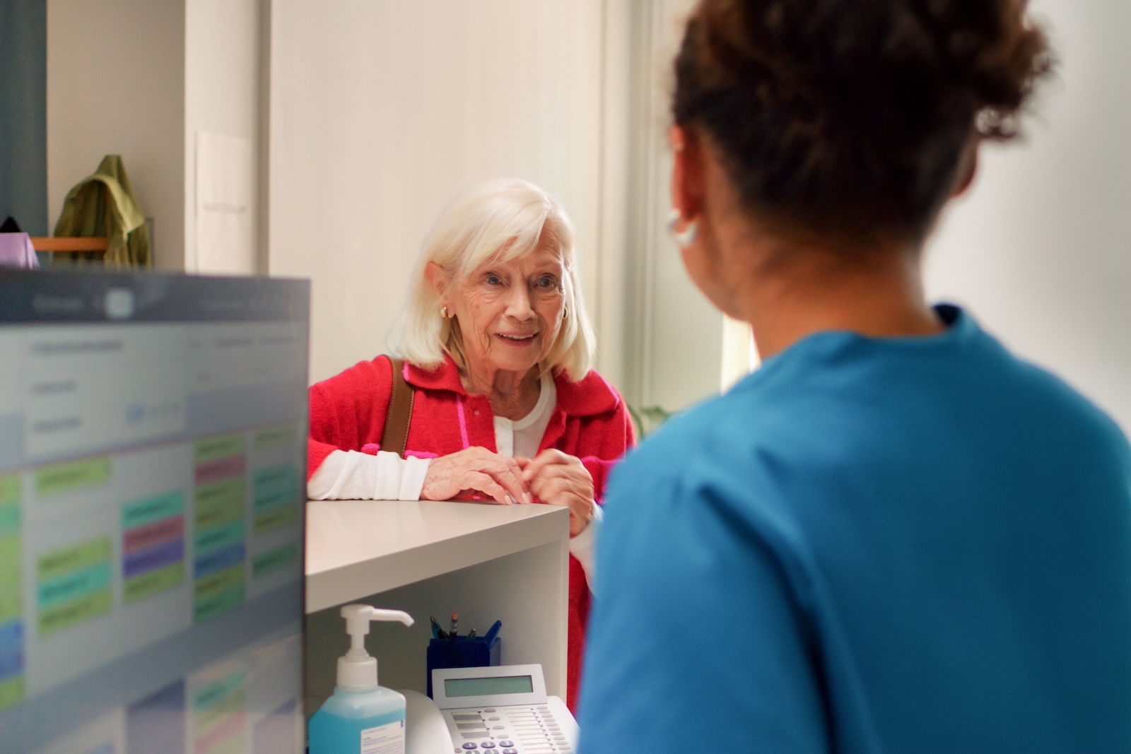 Ältere Patientin spricht mit einer medizinischen Fachkraft am Empfang einer Arztpraxis.